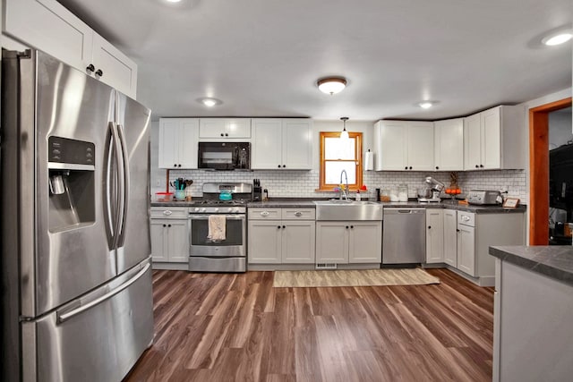 kitchen with appliances with stainless steel finishes, decorative backsplash, sink, white cabinetry, and dark hardwood / wood-style floors