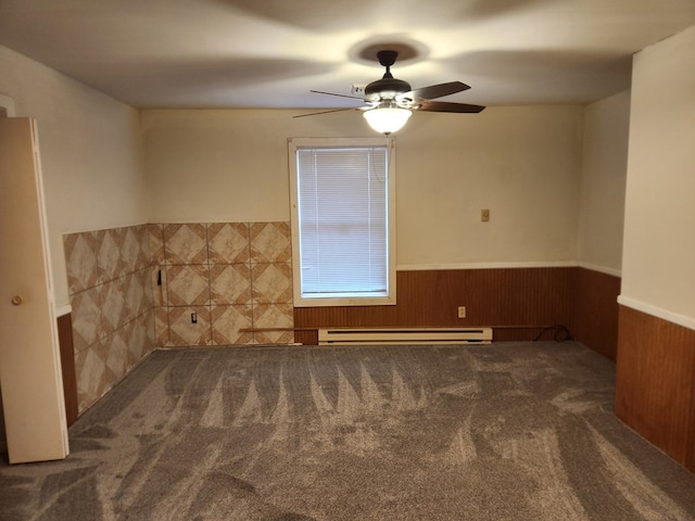 empty room with ceiling fan, wooden walls, carpet floors, baseboard heating, and wainscoting