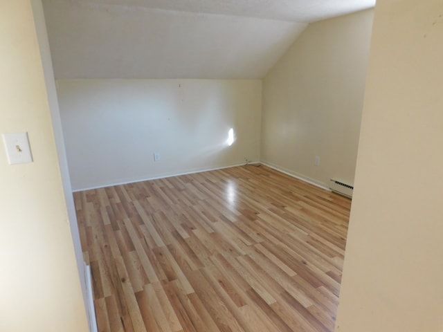 additional living space with a baseboard radiator, light wood-style flooring, and vaulted ceiling