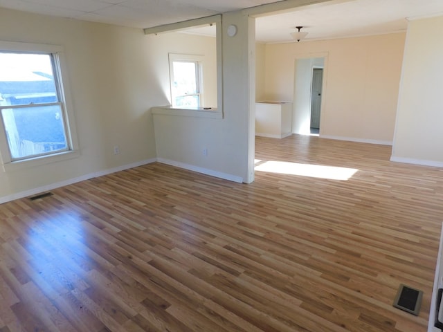 spare room featuring visible vents, a healthy amount of sunlight, baseboards, and wood finished floors