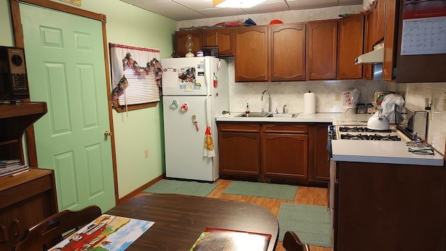 kitchen featuring tasteful backsplash, under cabinet range hood, light countertops, freestanding refrigerator, and a sink