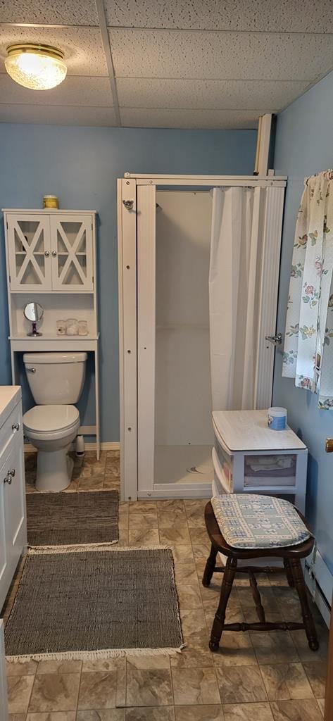 full bathroom featuring toilet, a stall shower, a paneled ceiling, baseboards, and vanity