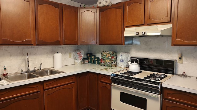 kitchen featuring range with gas cooktop, under cabinet range hood, light countertops, decorative backsplash, and a sink