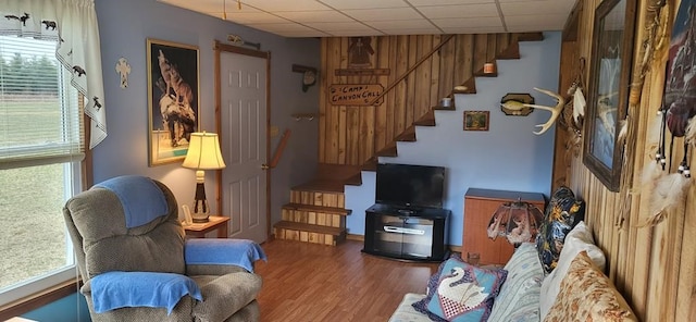 living area with stairway, plenty of natural light, a paneled ceiling, and wood finished floors