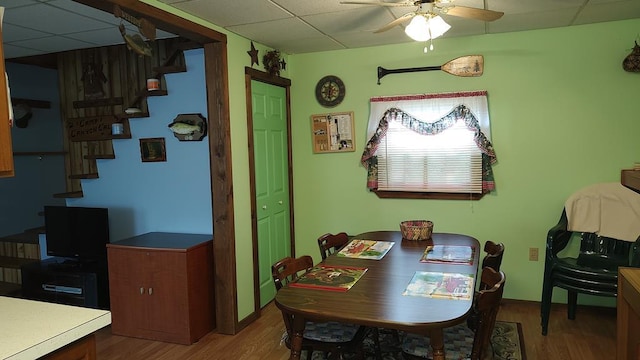 dining space with a drop ceiling, stairway, wood finished floors, and ceiling fan