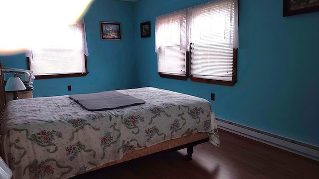 bedroom featuring multiple windows, a baseboard heating unit, and wood finished floors