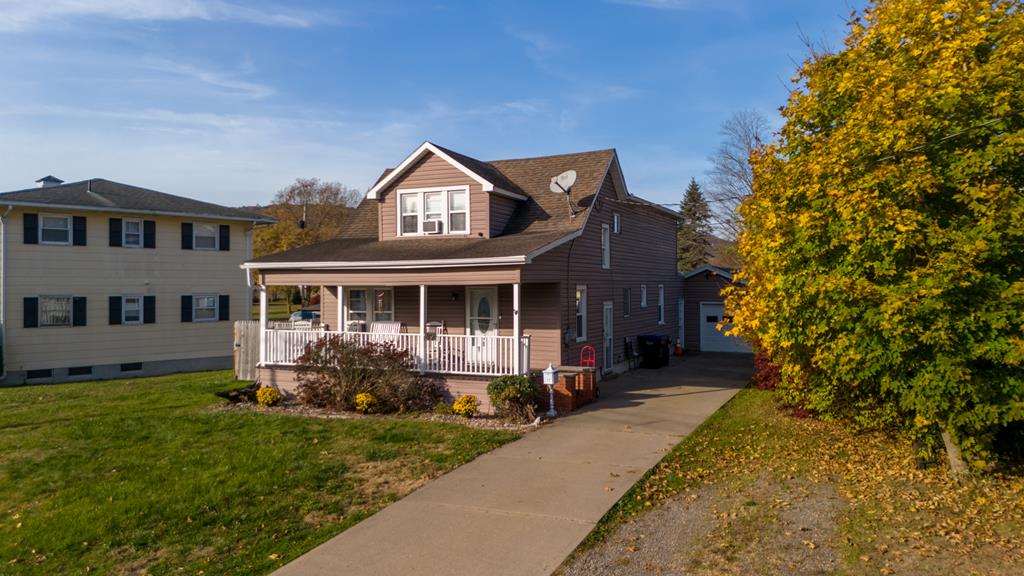 view of front of property featuring an outbuilding, covered porch, a front yard, and a garage