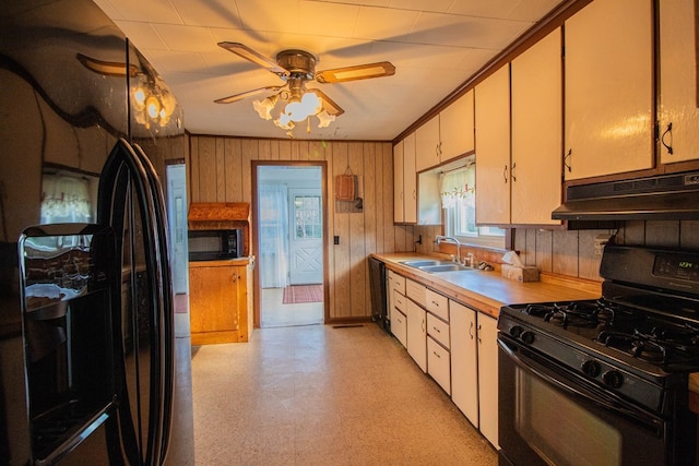 kitchen featuring ceiling fan, crown molding, sink, black appliances, and wood walls