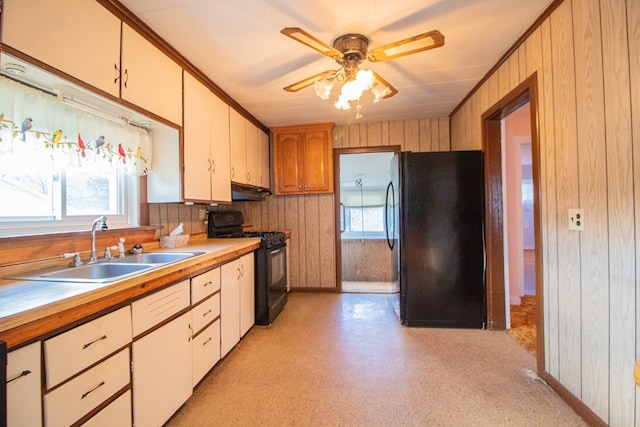 kitchen featuring a healthy amount of sunlight, wood walls, sink, and black appliances