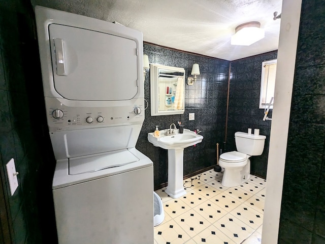 bathroom featuring sink, tile walls, stacked washer / dryer, tile patterned flooring, and toilet