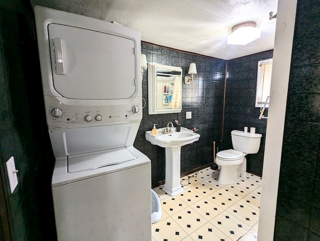 bathroom featuring tile patterned flooring, sink, toilet, and stacked washer / dryer