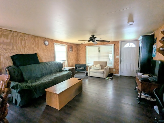 living room with ceiling fan, a healthy amount of sunlight, dark wood-type flooring, and wooden walls