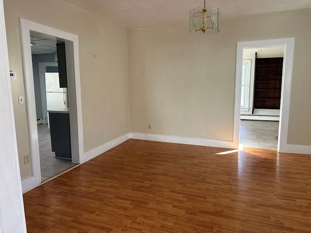 empty room featuring baseboard heating, hardwood / wood-style floors, and a notable chandelier