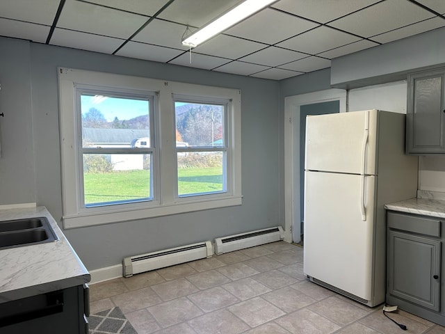 kitchen featuring gray cabinetry, a drop ceiling, white fridge, and a baseboard heating unit