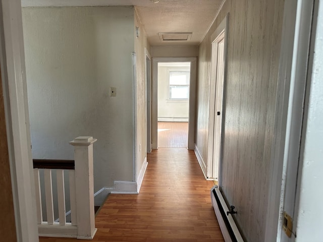 hall featuring light hardwood / wood-style flooring, a baseboard radiator, and a textured ceiling