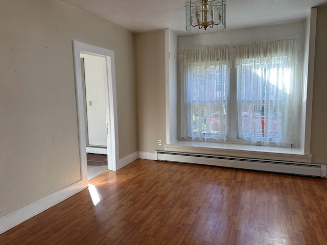 empty room with wood-type flooring, a baseboard heating unit, and a notable chandelier