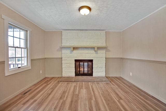 unfurnished living room featuring light hardwood / wood-style floors, a stone fireplace, and ornamental molding