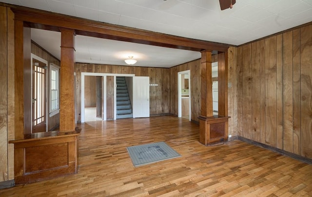 unfurnished living room featuring wood walls, hardwood / wood-style floors, ceiling fan, and decorative columns