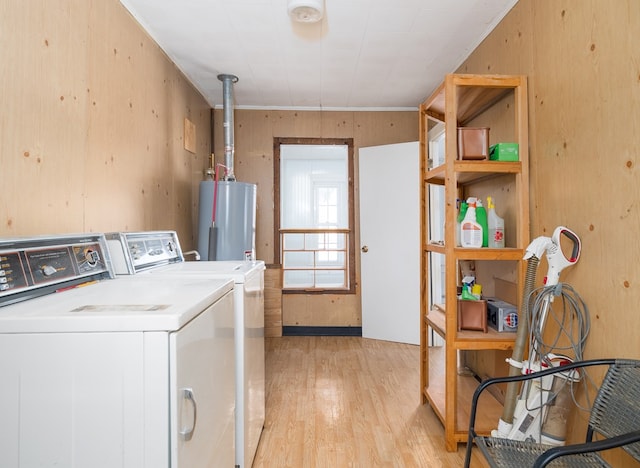 laundry room featuring washing machine and dryer, water heater, wooden walls, and light hardwood / wood-style floors