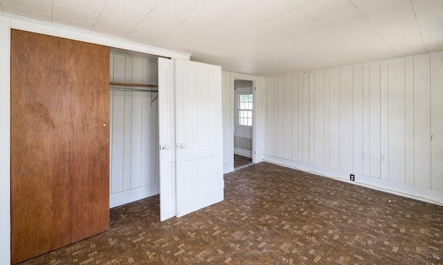 unfurnished bedroom with dark parquet flooring, wooden walls, and a closet