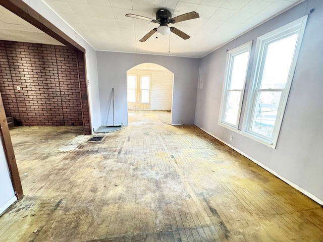 unfurnished room featuring ceiling fan, hardwood / wood-style floors, and brick wall