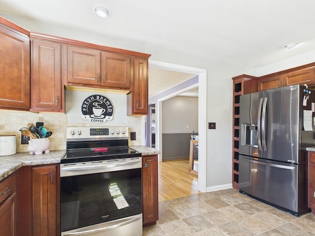 kitchen with light stone counters, baseboards, brown cabinets, appliances with stainless steel finishes, and tasteful backsplash