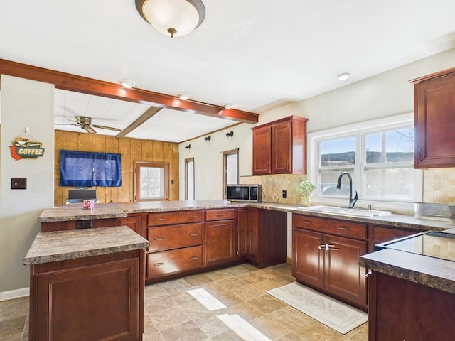 kitchen featuring a sink, stainless steel microwave, backsplash, and a peninsula