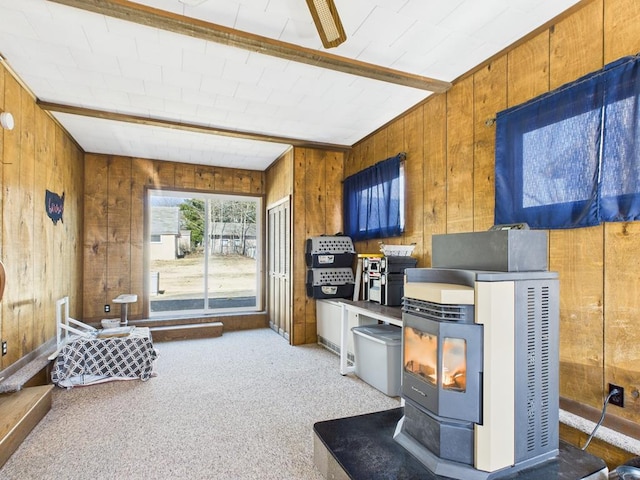 interior space featuring wooden walls, beam ceiling, a wood stove, light carpet, and brown cabinets