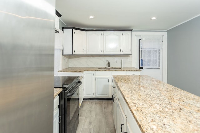 kitchen with stainless steel refrigerator, black range with electric stovetop, sink, light stone counters, and white cabinets