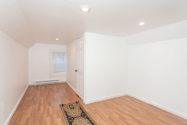 additional living space featuring lofted ceiling, light hardwood / wood-style flooring, and a baseboard heating unit