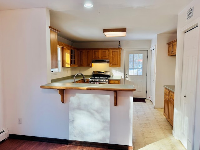 kitchen with kitchen peninsula, a baseboard radiator, a breakfast bar area, and gas range