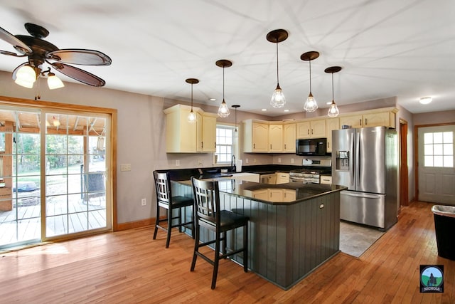 kitchen featuring ceiling fan, appliances with stainless steel finishes, decorative light fixtures, light hardwood / wood-style floors, and a kitchen bar