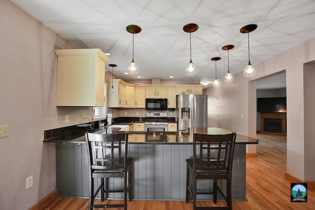 kitchen featuring hanging light fixtures, a kitchen breakfast bar, light hardwood / wood-style flooring, kitchen peninsula, and appliances with stainless steel finishes