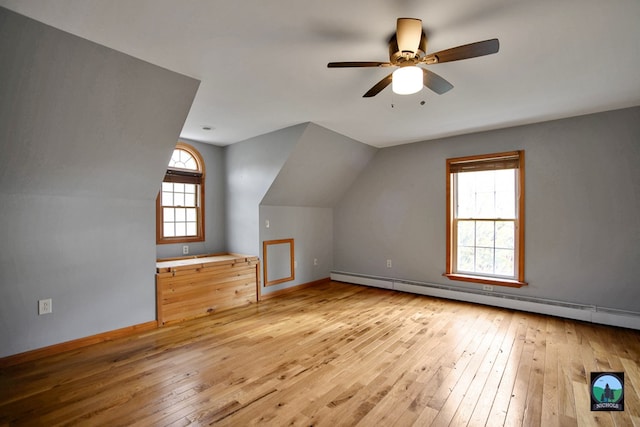 additional living space featuring ceiling fan, vaulted ceiling, light wood-type flooring, and a baseboard heating unit