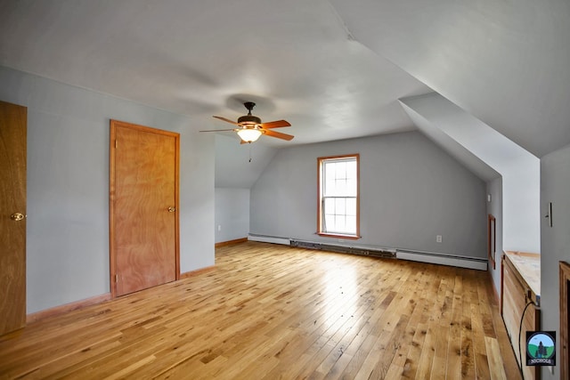 additional living space featuring ceiling fan, light hardwood / wood-style floors, vaulted ceiling, and a baseboard radiator