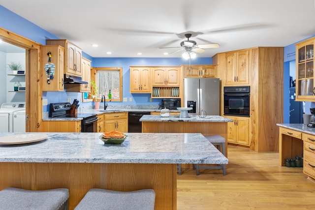 kitchen featuring light stone counters, black appliances, light hardwood / wood-style flooring, independent washer and dryer, and a center island