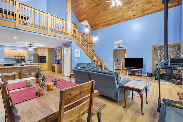 dining space with ceiling fan, high vaulted ceiling, wooden ceiling, light hardwood / wood-style floors, and a wood stove