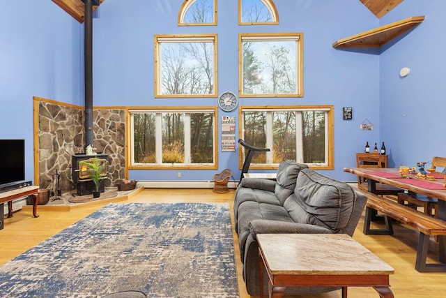 living room featuring high vaulted ceiling, a wood stove, a baseboard radiator, and light hardwood / wood-style flooring