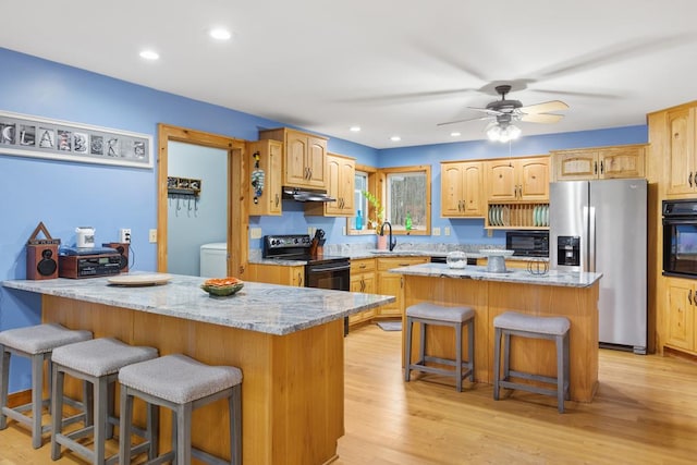 kitchen with light stone countertops, sink, a center island, light hardwood / wood-style flooring, and black appliances