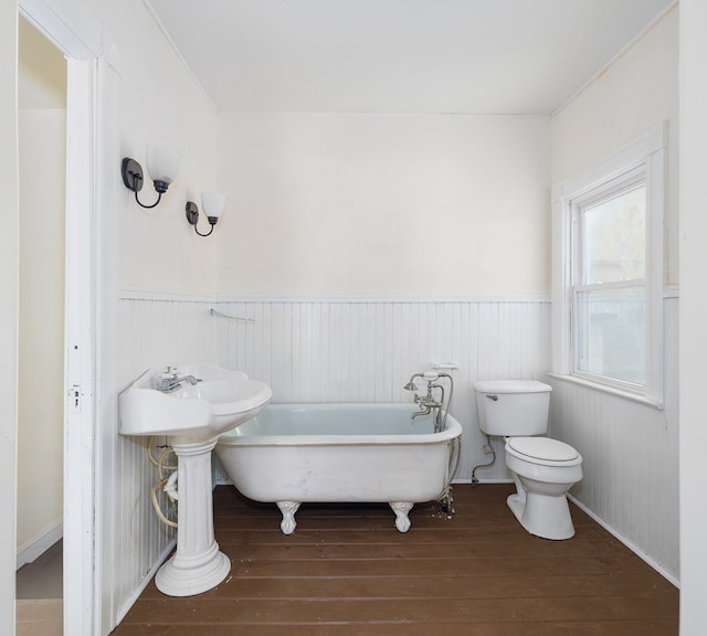 bathroom with a tub to relax in, wood-type flooring, and toilet