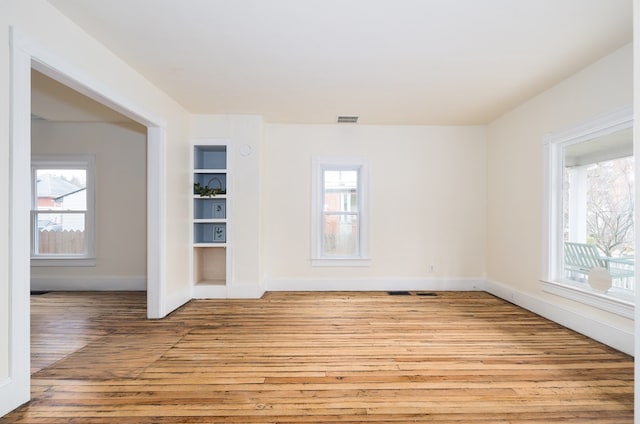 unfurnished room with built in features, plenty of natural light, and light wood-type flooring