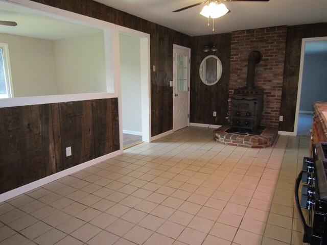 unfurnished living room with a wood stove, wood walls, light tile patterned flooring, and ceiling fan