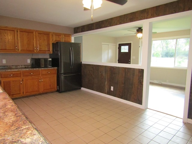 kitchen featuring black fridge, wooden walls, light tile patterned floors, and ceiling fan