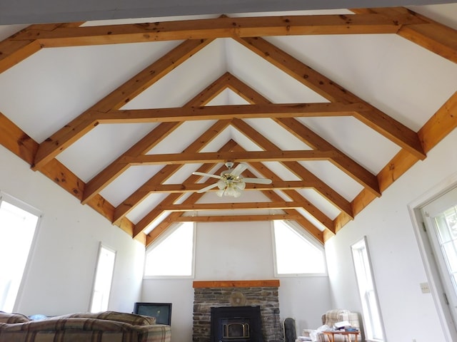 living room with ceiling fan, beam ceiling, a wood stove, and high vaulted ceiling