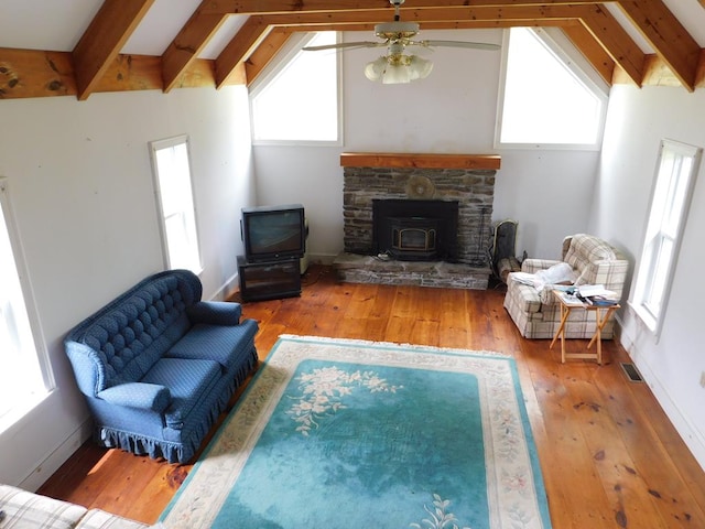 living room featuring a healthy amount of sunlight, a wood stove, ceiling fan, and lofted ceiling with beams