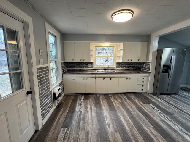 kitchen with dark wood-style flooring, stainless steel refrigerator with ice dispenser, open shelves, dark countertops, and a sink