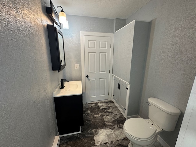 bathroom with toilet, marble finish floor, vanity, and a textured wall