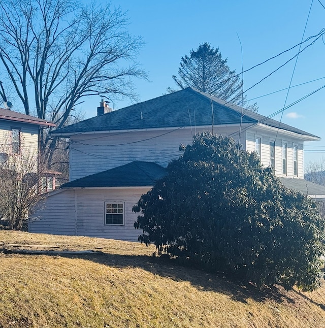 view of home's exterior featuring roof with shingles, a lawn, and a chimney