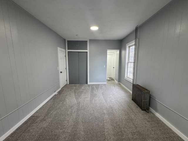 unfurnished bedroom featuring radiator heating unit, a closet, baseboards, and carpet flooring