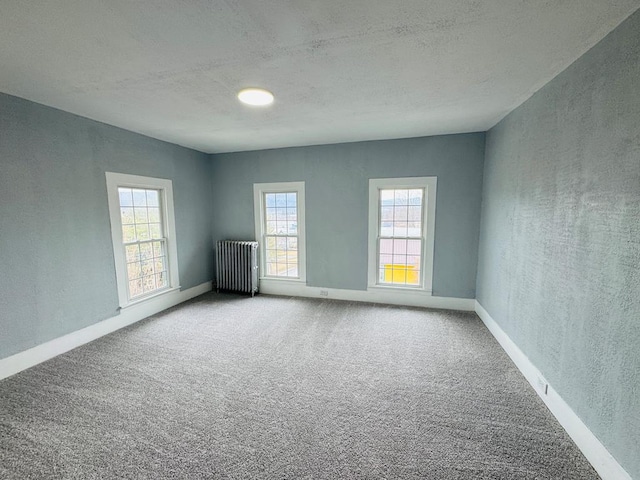 carpeted spare room featuring a textured wall, radiator heating unit, and baseboards